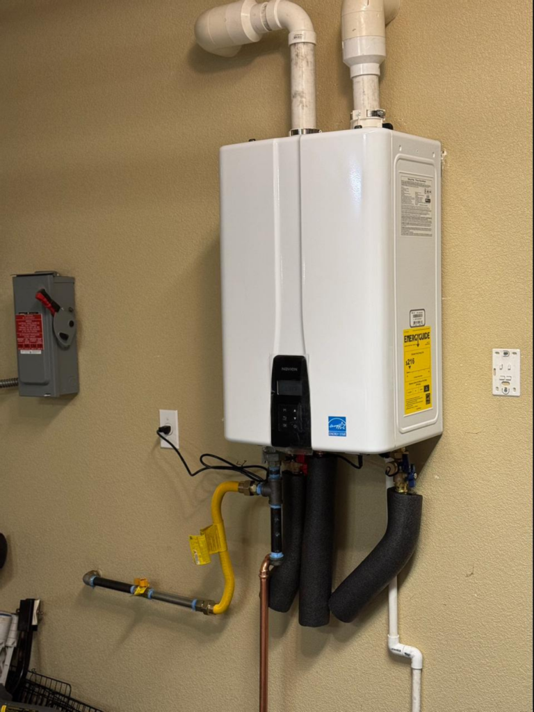 A Navien gas water heater installed on a light peach-colored wall.